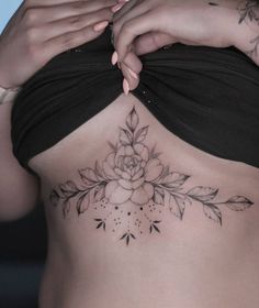 a woman's stomach with flowers and leaves tattooed on the side by her hands