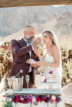 a bride and groom are cutting their wedding cake at an outdoor desert venue with mountains in the background