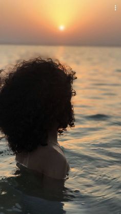 a woman in the water at sunset with her hair blowing back and looking off into the distance