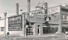 an old black and white photo of buildings in front of a building with signs on it