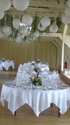 the tables are set up with white linens and paper lanterns hanging from the ceiling