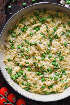 a pot filled with pasta and peas on top of a wooden table next to tomatoes