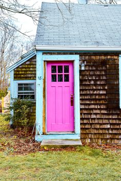 a pink door sits in front of a small wooden building with shingled roof and windows