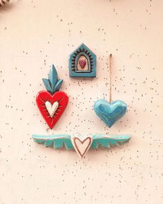 three heart shaped ornaments hanging on the wall next to each other, one with an angel's wing