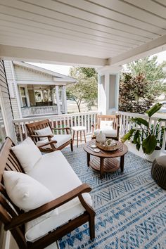 a porch with chairs, tables and pillows on the front porch overlooking an outdoor living area