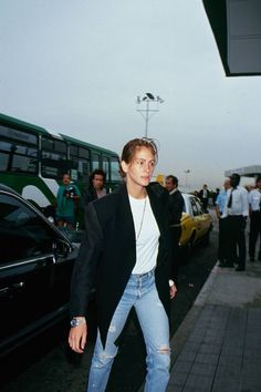 a woman in ripped jeans and a white shirt is walking down the street with her hand on her hip