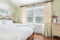 a white bed sitting under a window next to a wooden dresser with drawers underneath it