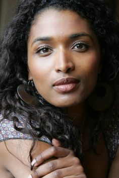 a close up of a woman with curly hair and earrings on her head looking at the camera