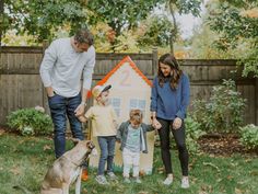 a family with two children and a dog in front of a house made out of cardboard