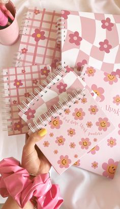 a hand holding a pink notebook with flowers on it, next to some other items