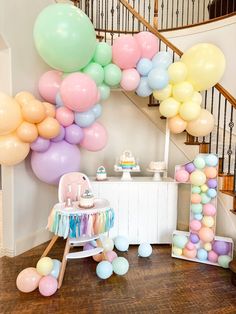 a baby's first birthday party with pastel balloons on the staircase and cake table