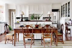 a kitchen with white cabinets and wooden table surrounded by four chairs in front of an island