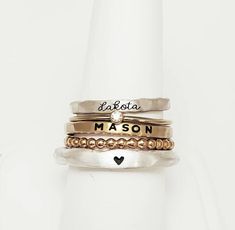 Personalized stackable ring set, engraved with names, a date, or a special word.  Metal: .999 fine silver, 14k gold filled, and 14k rose gold filled Dimensions: Name rings and beaded ring are 2mm tall on average, but our rings are handmade so variations will occur. Birthstone is 2mm on a 1mm band. The silver ring is a chunky organic style and is 3mm. Font: lowercase cursive, uppercase bold block, and lowercase typewriter (if you want a word instead of a heart on the silver ring) Unsure what size Heirloom Sterling Silver Stackable Jewelry, Gold Sterling Silver Initial Stackable Ring, Gold Sterling Silver Stackable Initial Ring, Adjustable Stackable Rings With Custom Name, Adjustable Stackable Initial Ring As Gift, Adjustable Stackable Jewelry For Anniversary, Custom Name Adjustable Stackable Rings, Personalized Gold Midi Rings In Sterling Silver, Silver 14k Gold Stackable Initial Ring