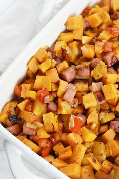 a white casserole dish filled with sweet potatoes and ham