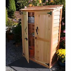 a wooden storage shed with its doors open and flowers in the back ground behind it