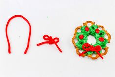 a cookie decorated like a christmas wreath next to a pair of red hair ties and a green pretzel