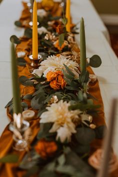 a long table with candles and flowers on it is decorated in gold, orange and white