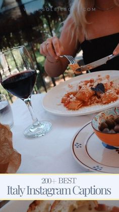 a woman sitting at a table eating food with a glass of wine in front of her