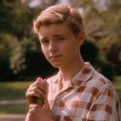 a young man is holding an umbrella in the park while wearing a plaid shirt and looking at the camera