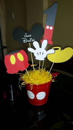 a mickey mouse centerpiece in a red bucket with yellow straws on the table