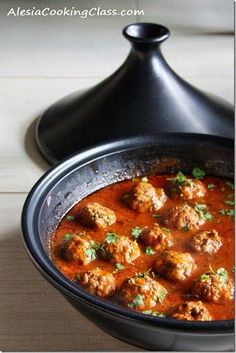 a black pot filled with meatballs covered in tomato sauce and garnished with parsley