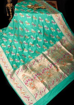 This teal Banarasi Katan silk saree with Meenakari Peacock design Motifs and Paithani style tissue and meena Borders and pallu add elegance and style to the overall look. Perfect for special occasions, this saree tells tall tales of craftsmanship! SILK MARK CERTIFIED This saree is ready to wear with fall and pico done. Handmade silk tassels adorn the pallu and add more grace to it. An unstitched blouse fabric is included. *Note: There may be minor variations in the shade, the texture of the product. Hues/textures show differently due to variations in screen settings and other factors, *Note: This is a handwoven saree and there may be slight inconsistencies such as in it's weaving. These are characteristic of handmade products and attest to their originality and are not considered as defect Banarasi Katan Silk Saree, Peacock Motifs, Design Motifs, Silk Tassels, Katan Silk Saree, Tall Tales, Saree Blouses, Katan Silk, Peacock Design