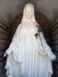 a statue of the virgin mary holding a rose in it's hand and wearing a white dress