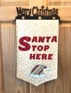 a christmas banner hanging on a door with santa's top here written in red