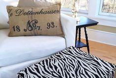 a zebra print ottoman sitting next to a white couch with a black and white pillow