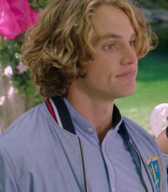 a man with long curly hair holding a cell phone in his right hand and looking off into the distance