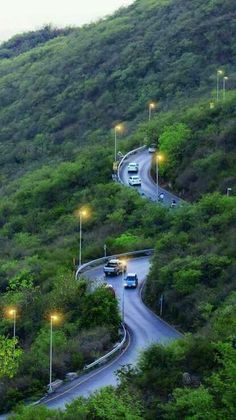 cars driving down a winding road surrounded by lush green hills and trees on the side