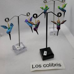 three metal birds are on display in front of a sign that says los colibris