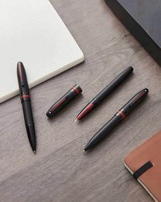 four different pens sitting on top of a desk next to an open notebook and pen