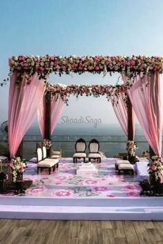 an outdoor wedding set up with pink drapes and flowers on the floor, overlooking the ocean