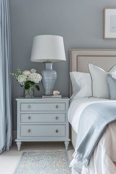 a bedroom with a bed, nightstand and flowers on the night stand in front of it