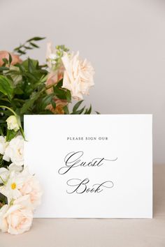 a white card with the words guest book on it sitting next to some pink and white flowers