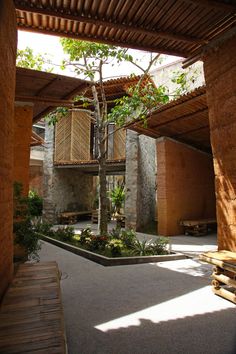 an indoor courtyard with trees and benches in the middle, surrounded by stone walls and wooden slatted roofing