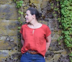 a woman standing in front of a stone wall with ivy growing on it's sides