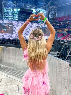 a girl in a pink dress at a concert with her hands up to the sky