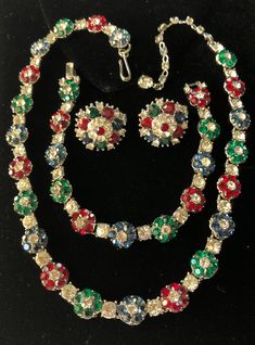 "Here is a very lovely vintage necklace, bracelet and earrings set designed by Trifari. This jewelry is beautifully fashioned in a floral pattern with glittering rhinestones in jewel tones of emerald green, sapphire blue, ruby red and brilliantly clear tones. The stone setting is in silver tone metal. The necklace has a hook and adjustable extension strand for a custom fit while the bracelet has a flip over clasp for closure. The earrings are in a clip-on style. The necklace measures 16\" from e Rhinestone Costumes, Vintage Jewelry Sets, Trifari Jewelry, Vintage Trifari, Vintage Style Jewellery, Pretty Necklaces, Antique Necklace, Pretty Bracelets, Green Sapphire