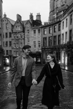 a man and woman holding hands while walking down a cobblestone street in an old european city