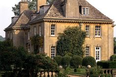 an old house with many windows and bushes around it's perimeter in the country side