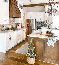 a kitchen decorated for christmas with white cabinets and wood flooring, potted tree in the center