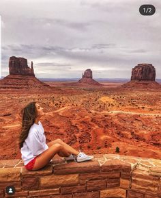 a woman sitting on top of a brick wall next to a desert area with mountains in the background