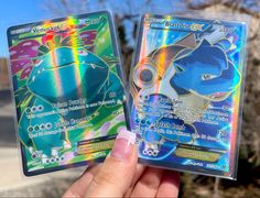 someone is holding two pokemon cards in their hand, both have different designs on them