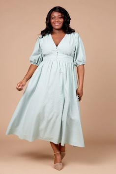 a woman in a light blue dress poses for the camera with her hands on her hips