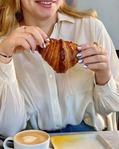 a woman sitting at a table with a cup of coffee and a croissant