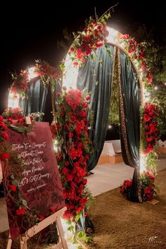 an outdoor ceremony with red flowers and greenery on the arch, along with a chalkboard sign