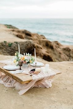 a table set up on the beach with flowers and candles