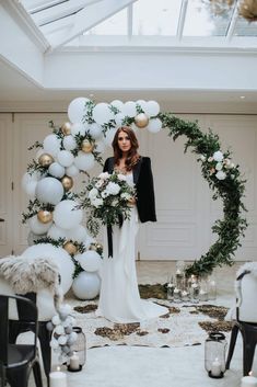 a woman standing in front of a white arch with balloons and greenery on it